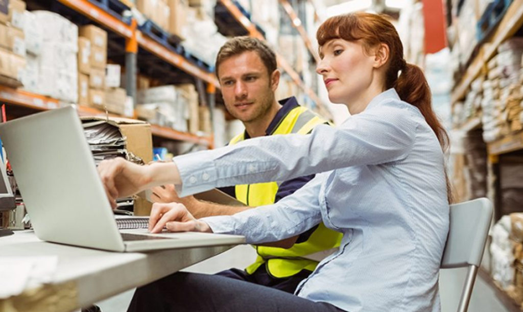 This image depicts a warehouse manager working at a laptop computer along with one of the employees.