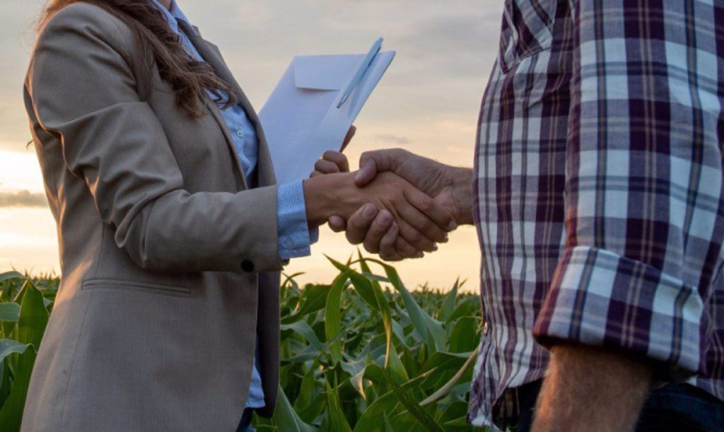 This image depicts two people in a farm field shaking hands