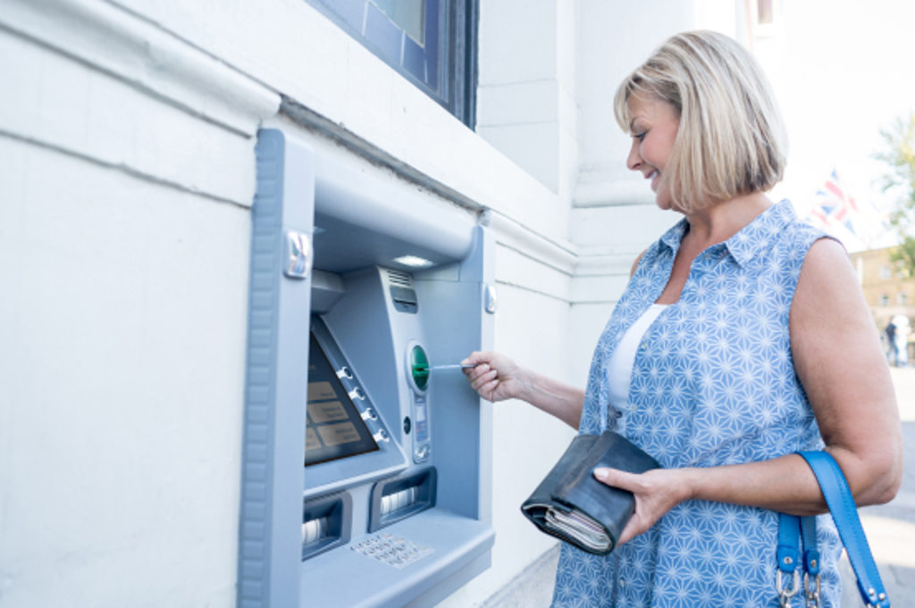 This image depicts a woman placing her debit card into an ATM.