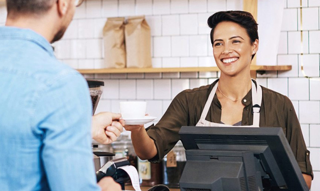 Image depicts a barista cashier handing a cup of coffee to a customer