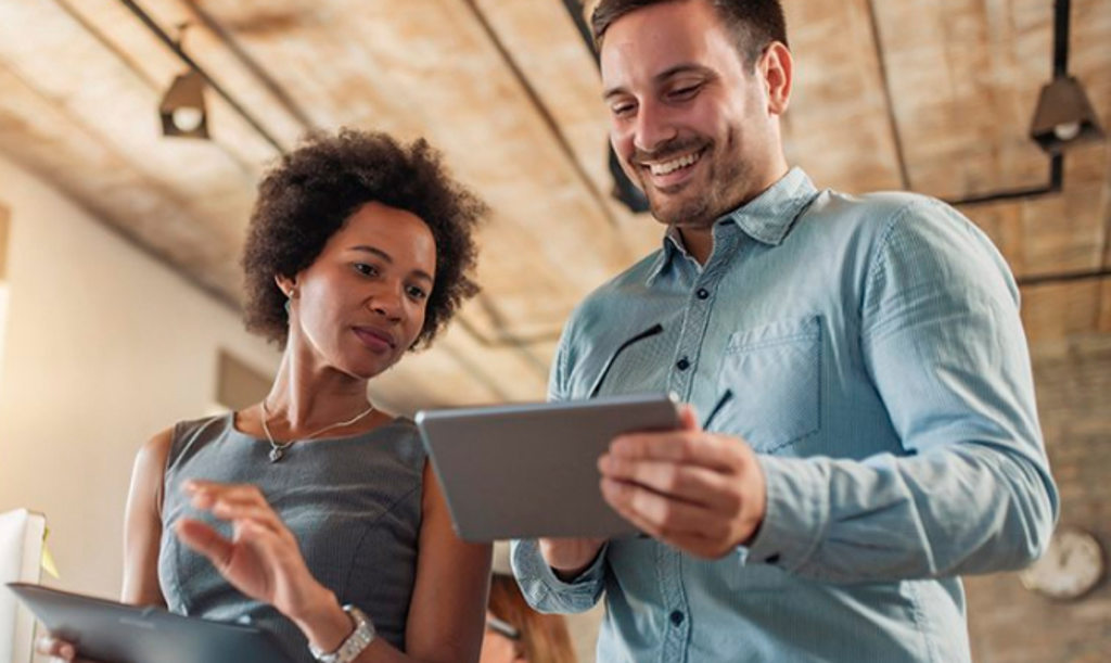 This image depicts two coworkers smiling and looking at tablet computers.