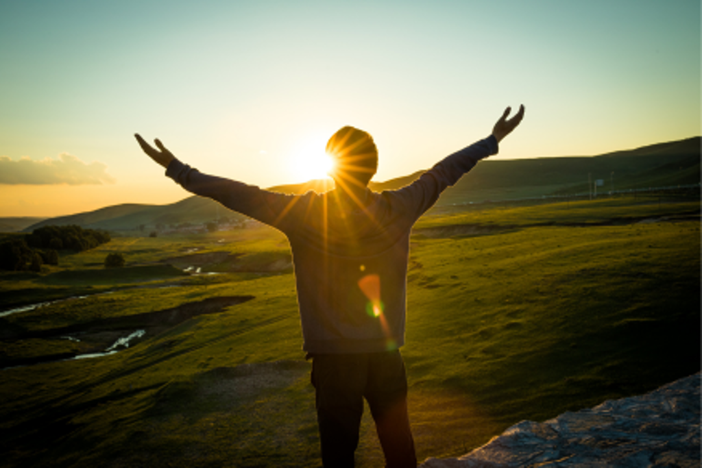 man with arms in air looking at sunset